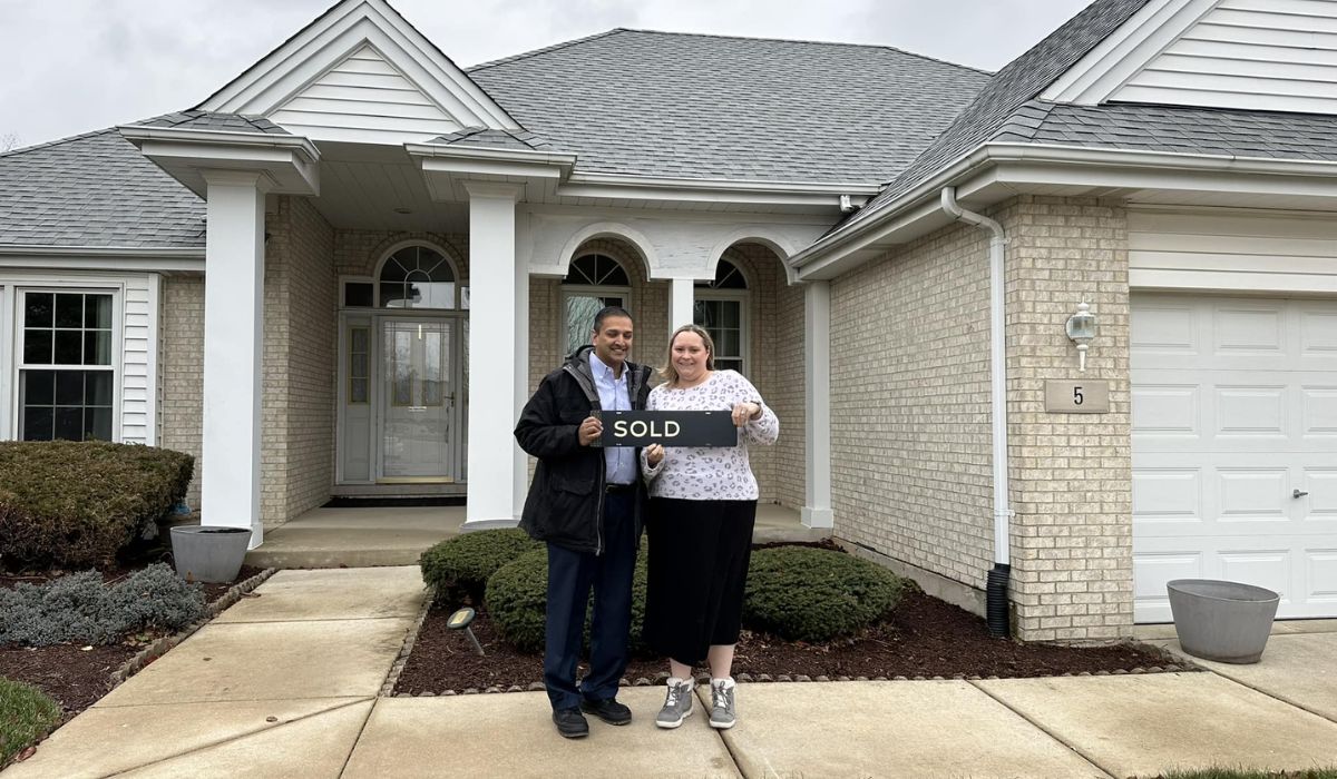 A couple standing in front of the house they bought with a "sold" sign